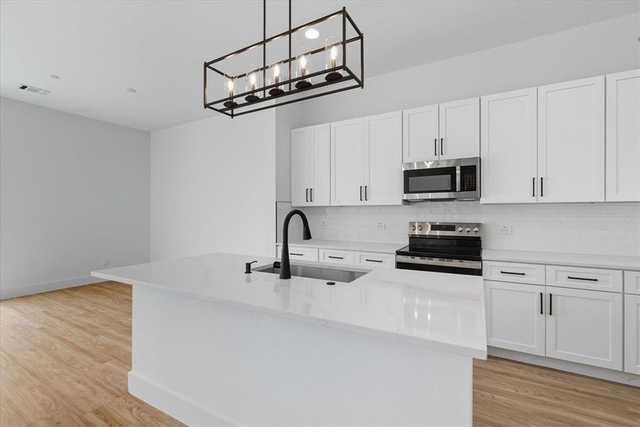 Kitchen with white cabinets, an island with sink, stainless steel appliances, decorative backsplash, and light wood-style floors