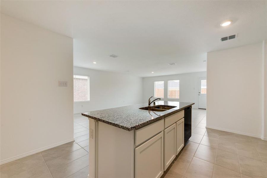 Kitchen with an island with sink, light stone countertops, sink, dishwasher, and light tile patterned floors