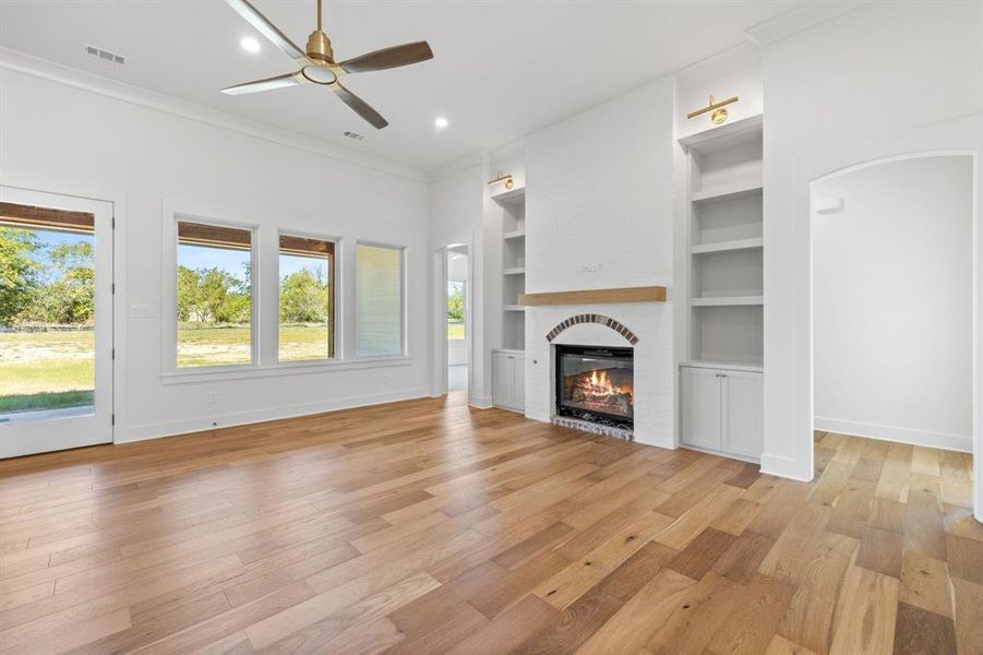 Unfurnished living room with built in shelves, light hardwood / wood-style flooring, crown molding, and ceiling fan