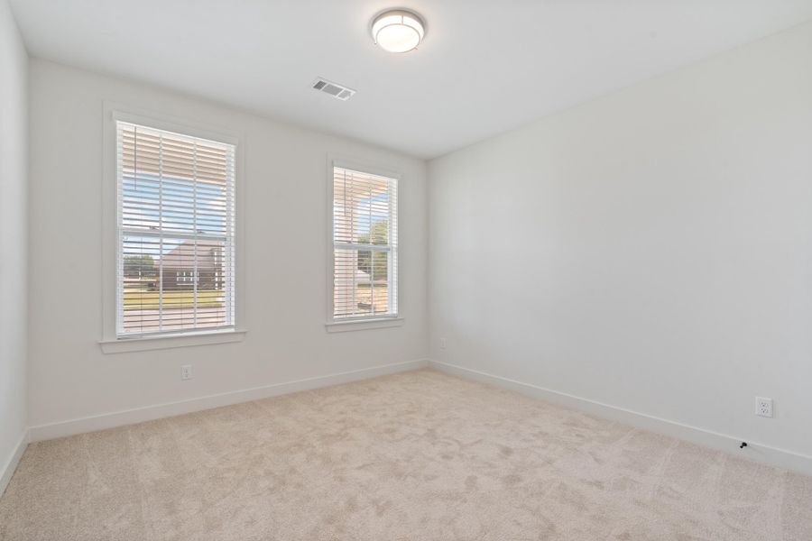 Neutral tone carpet flooring, white painted walls, two windows with blinds, and an overhead flush mount light fixture Neutral tone carpet flooring, white painted walls, two windows with blinds, and an overhead flush mount light fixture