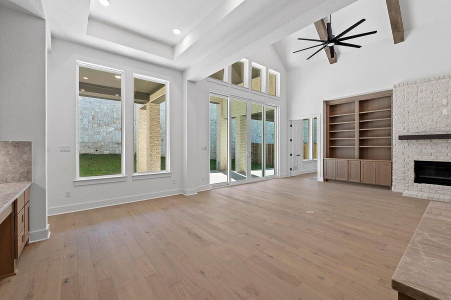 Unfurnished living room with a glass covered fireplace, light wood-style flooring, ceiling fan, recessed lighting, and a towering ceiling Unfurnished living room with a glass covered fireplace, light wood-style flooring, ceiling fan, recessed lighting, and a towering ceiling