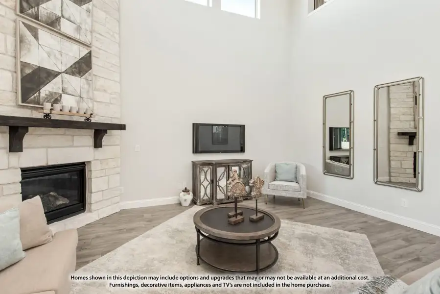 Living room with two-story ceiling, stone fireplace, hardwood floors, and wall-mounted TV