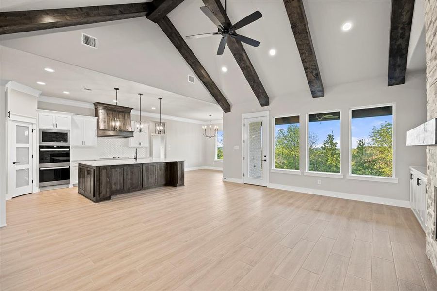 Unfurnished living room with recessed lighting, beam ceiling, a chandelier, high vaulted ceiling, and light wood finished floors
