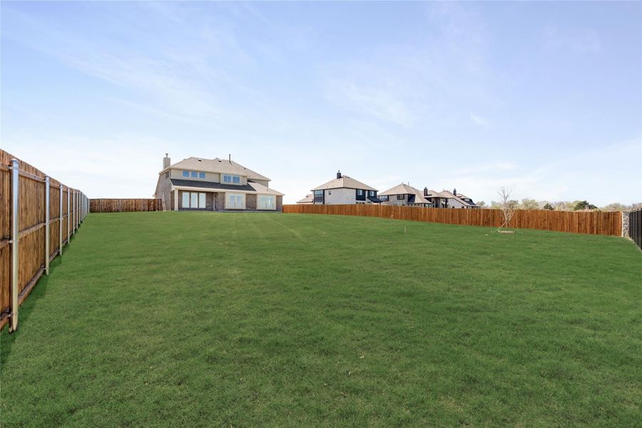 Large backyard with green lawn, wood privacy fence, and two-story brick home in background Large backyard with green lawn, wood privacy fence, and two-story brick home in background