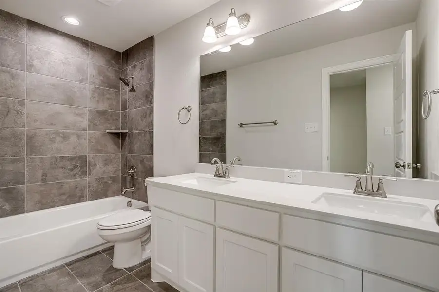 Full bathroom with double vanity, shower / bathtub combination, recessed lighting, and dark tile patterned flooring