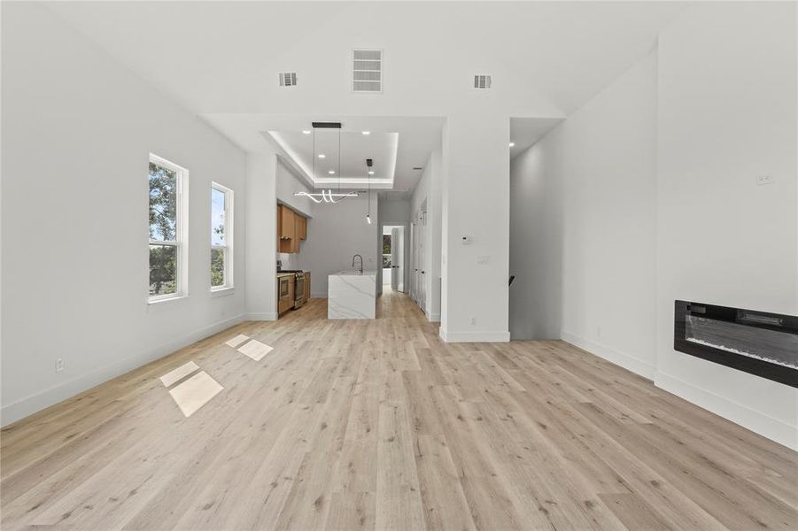 Unfurnished living room with a tray ceiling, light wood-type flooring, recessed lighting, and a glass covered fireplace