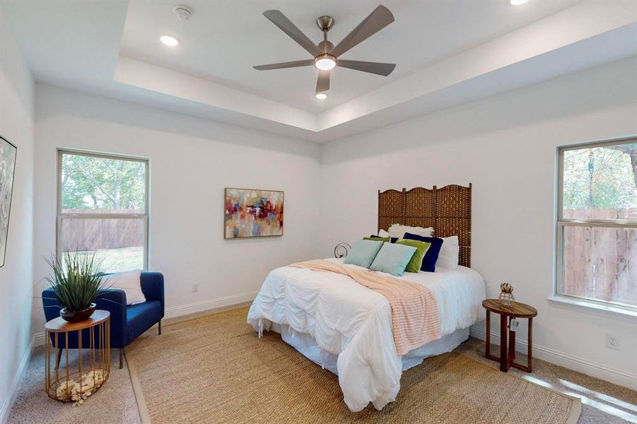 Main Carpeted bedroom with ceiling fan and a raised ceiling