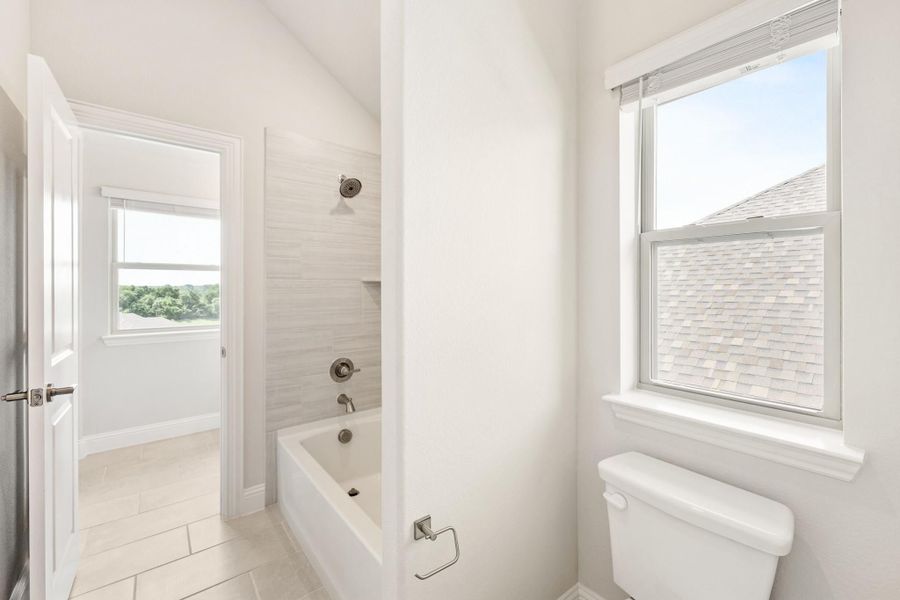Bright white bathroom with soaking tub, tiled shower surround, toilet, and two windows