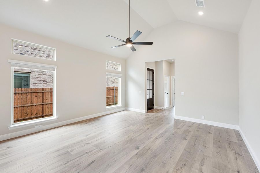 Empty living room with vaulted ceiling, ceiling fan, light wood floors, and large windows