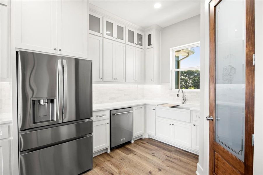 Kitchen with appliances with stainless steel finishes, glass insert cabinets, white cabinetry, light wood finished floors, and recessed lighting Kitchen with appliances with stainless steel finishes, glass insert cabinets, white cabinetry, light wood finished floors, and recessed lighting