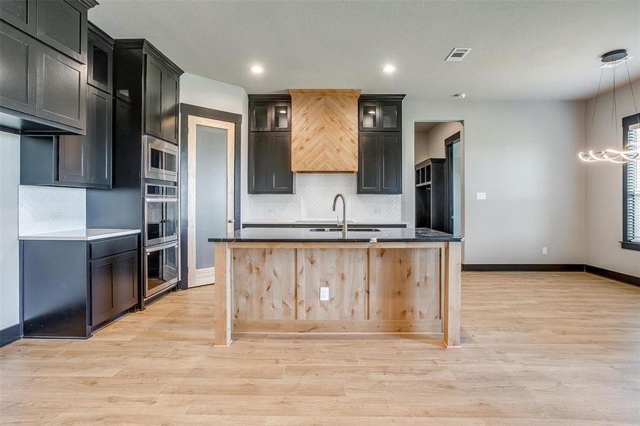 Kitchen featuring stainless steel microwave, backsplash, a center island with sink, sink, and light hardwood / wood-style flooring