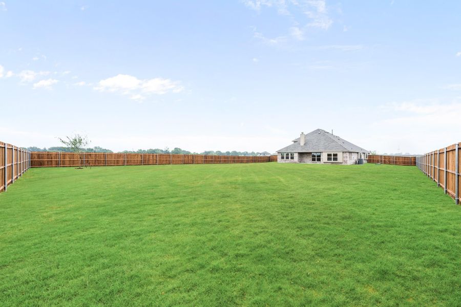 Large backyard with green grass, wood privacy fence, and brick home visible in background