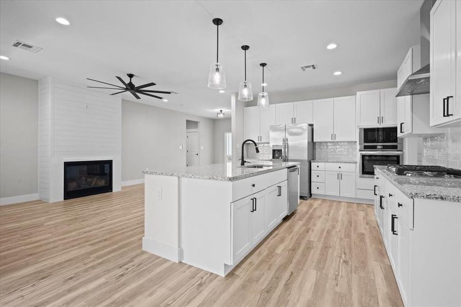 Kitchen with appliances with stainless steel finishes, ceiling fan, decorative backsplash, white cabinetry, and light wood-type flooring