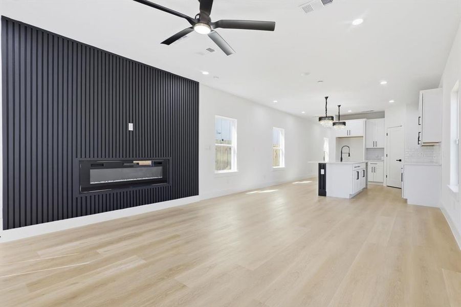 Unfurnished living room featuring light wood-style floors, a glass covered fireplace, ceiling fan, and recessed lighting