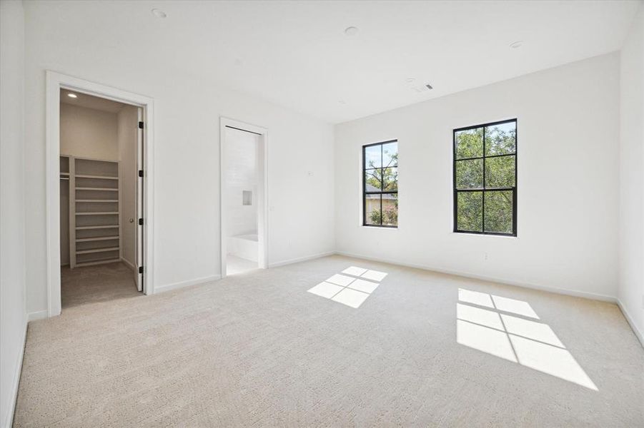 This secondary bedroom features soft carpeting and two large windows that fill the space with natural light. The room includes direct access to an ensuite bathroom and a spacious walk-in closet, offering ample storage and convenience.