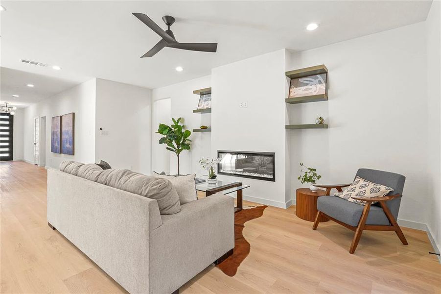 Living room with light wood-style floors, a glass covered fireplace, recessed lighting, and ceiling fan