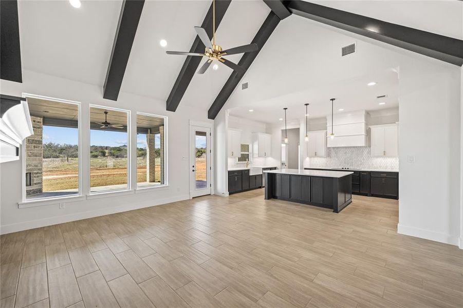 Dual tone kitchen featuring open floor plan, a center island, light countertops, ceiling fan, and pendant lighting