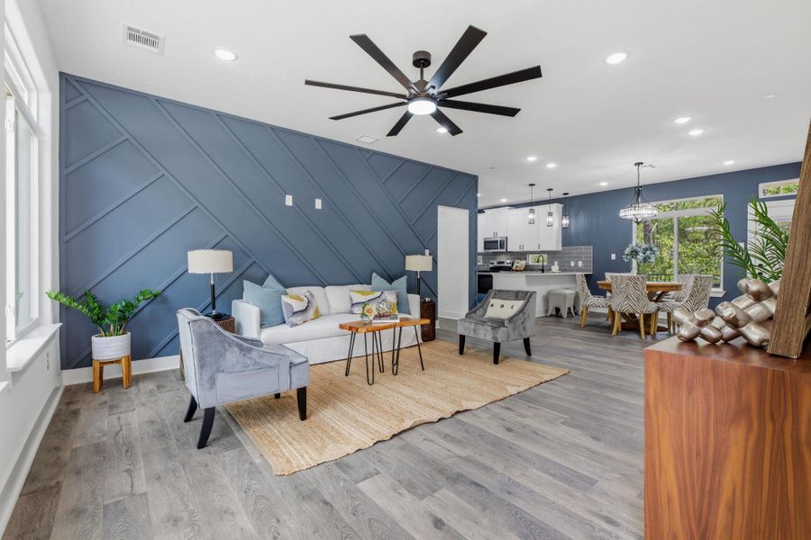 An open concept living and dining space features a stylish accent wall and light flooring.