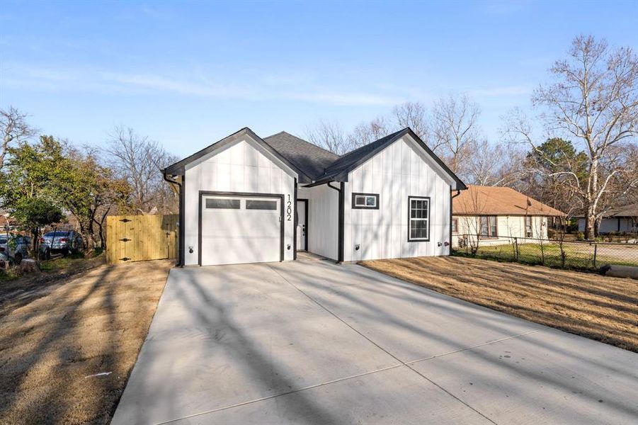 Modern farmhouse featuring driveway, a gate, and an attached garage
