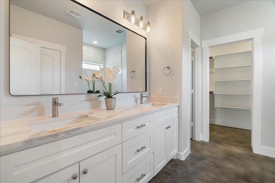 Dual vanities, a framed mirror, and bright light fixtures grace the primary bathroom. Dual vanities, a framed mirror, and bright light fixtures grace the primary bathroom.
