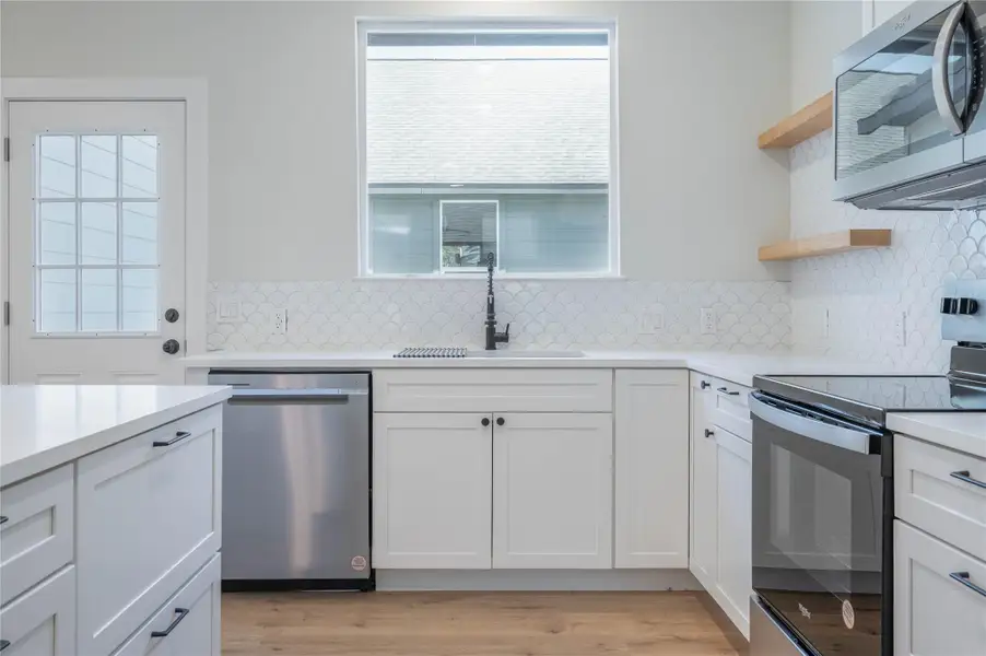 Kitchen with stainless steel appliances, decorative backsplash, open shelves, light countertops, and white cabinets