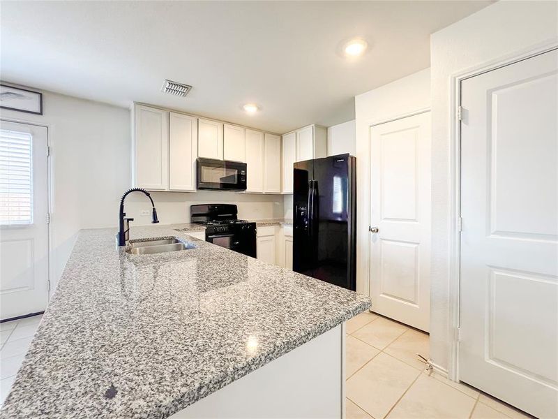 Kitchen featuring black appliances, light stone counters, white cabinets, a peninsula, and light tile patterned floors