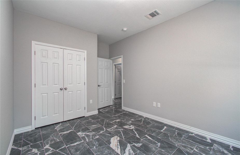 This room features sleek, dark marble flooring and neutral gray walls, offering a modern and clean aesthetic. It includes a double-door closet for ample storage and an entrance door, making it ideal for a bedroom or office space.
