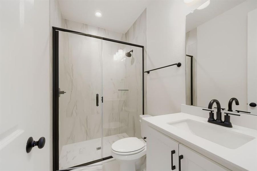Contemporary bathroom featuring a frameless glass shower enclosure with matte black hardware, white vanity with integrated sink, and coordinating matte black faucet