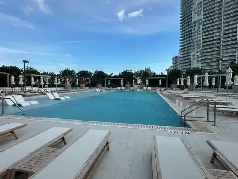 Swimming pool featuring a tiled deck, metallic handrails, perimeter lighting, and shaded structural cabanas Swimming pool featuring a tiled deck, metallic handrails, perimeter lighting, and shaded structural cabanas