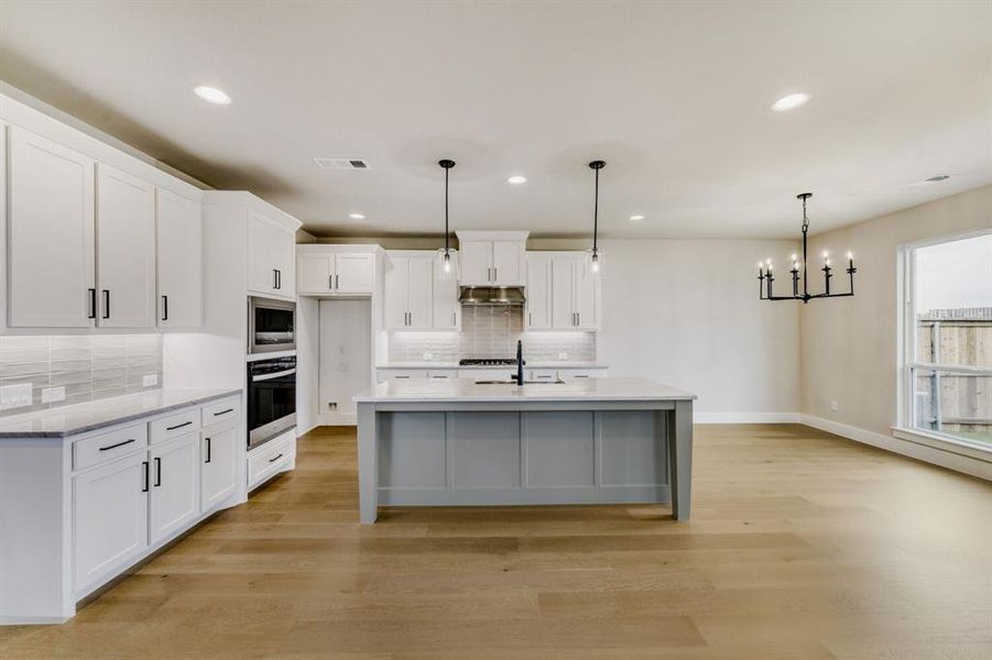 Modern kitchen featuring light wood-finish flooring, white cabinetry with matte black hardware, light-toned countertops, and a subway tile backsplash
