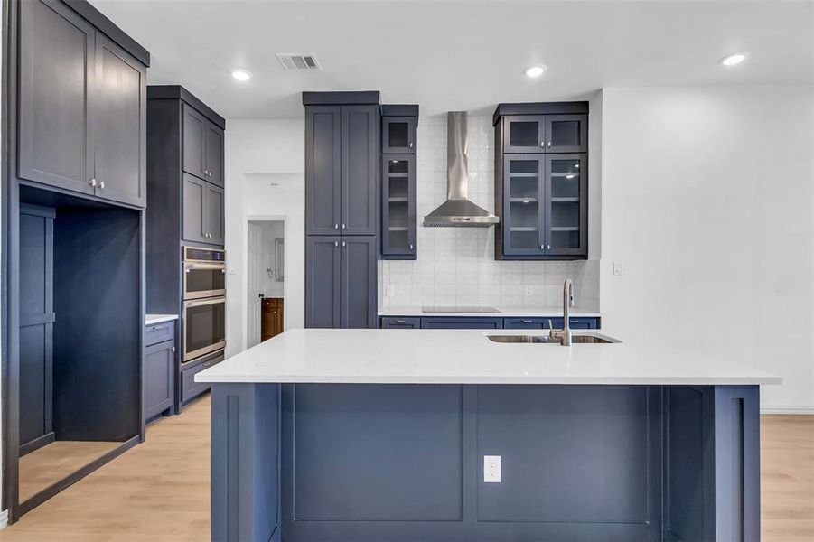 Kitchen with light wood-type flooring, wall chimney range hood, backsplash, and black electric cooktop