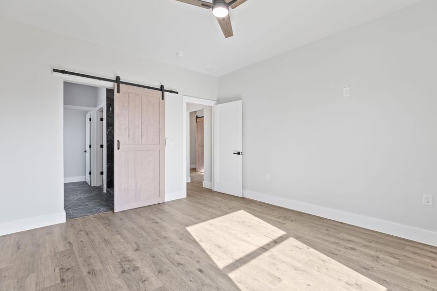 Unfurnished bedroom featuring a barn door, light wood finished floors, and ceiling fan