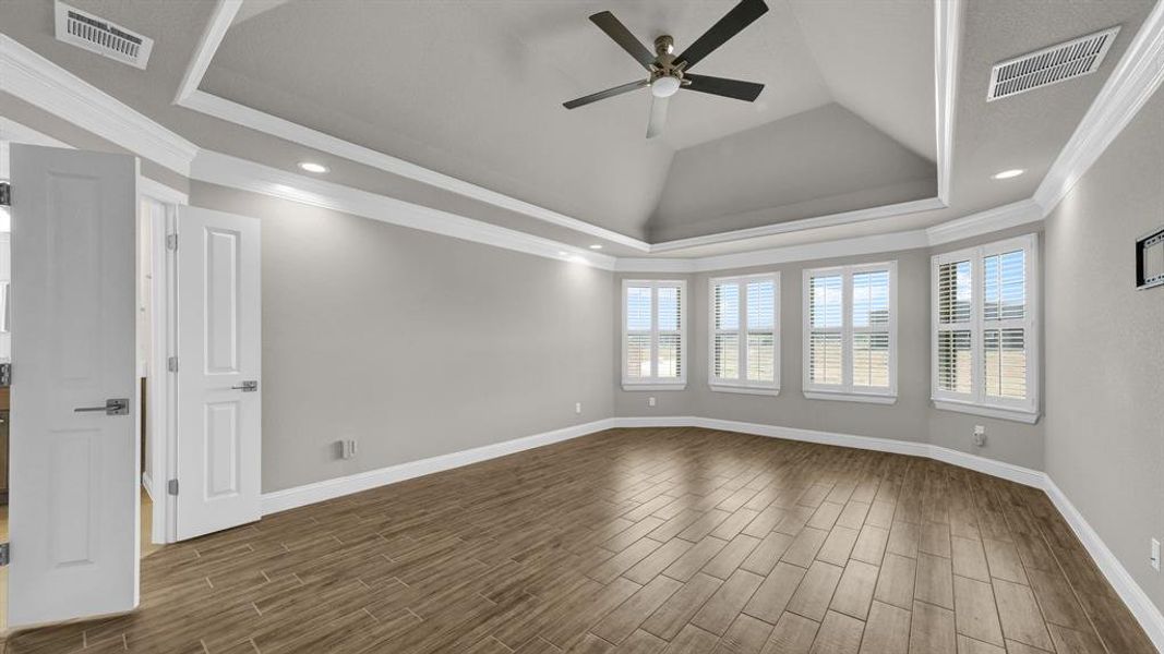 Primary bedroom featuring a tray ceiling, dark wood-type flooring, ornamental molding, lofted ceiling, and ceiling fan