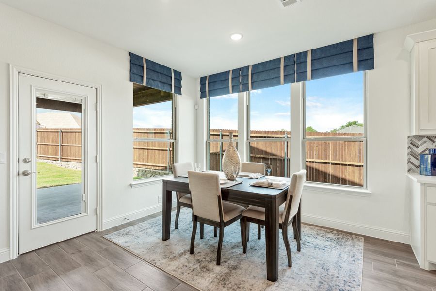 Breakfast nook with dark wood table, four chairs, blue roman shades, and glass door to backyard