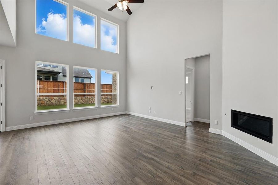 Unfurnished living room featuring a high ceiling, a ceiling fan, healthy amount of natural light, dark wood finished floors, and baseboards Unfurnished living room featuring a high ceiling, a ceiling fan, healthy amount of natural light, dark wood finished floors, and baseboards