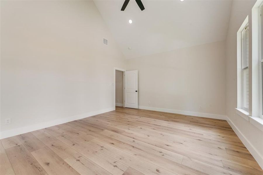 Spacious room featuring wood-finish flooring, vaulted ceilings, recessed lighting, a ceiling fan, and multiple windows