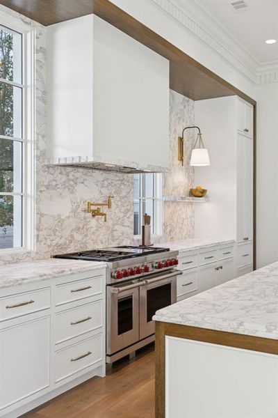 Kitchen with custom exhaust hood, white cabinetry, range with two ovens, and healthy amount of natural light