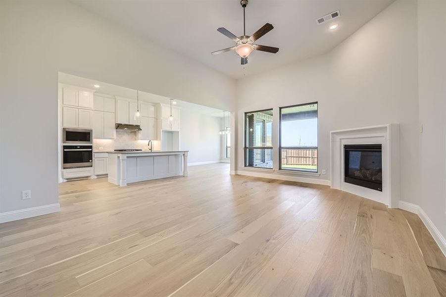 Unfurnished living room with ceiling fan, sink, light hardwood / wood-style floors, and a high ceiling