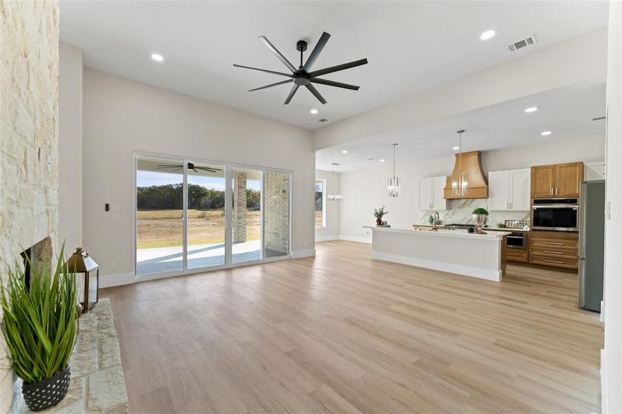 Unfurnished living room with ceiling fan, light wood finished floors, a fireplace, recessed lighting, and a chandelier Unfurnished living room with ceiling fan, light wood finished floors, a fireplace, recessed lighting, and a chandelier