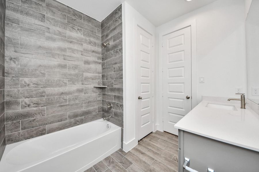 Secondary bath features tile flooring, bath/shower combo with tile surround, light stained wood cabinets, beautiful light countertop.