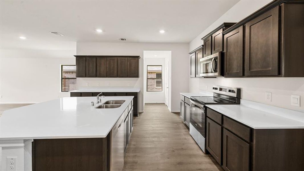 Kitchen featuring dark wood-finish cabinetry, light countertops, stainless steel appliances, and wood-finish flooring Kitchen featuring dark wood-finish cabinetry, light countertops, stainless steel appliances, and wood-finish flooring