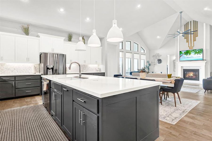 Kitchen with high vaulted ceiling, a glass covered fireplace, decorative light fixtures, backsplash, and light wood-type flooring Kitchen with high vaulted ceiling, a glass covered fireplace, decorative light fixtures, backsplash, and light wood-type flooring