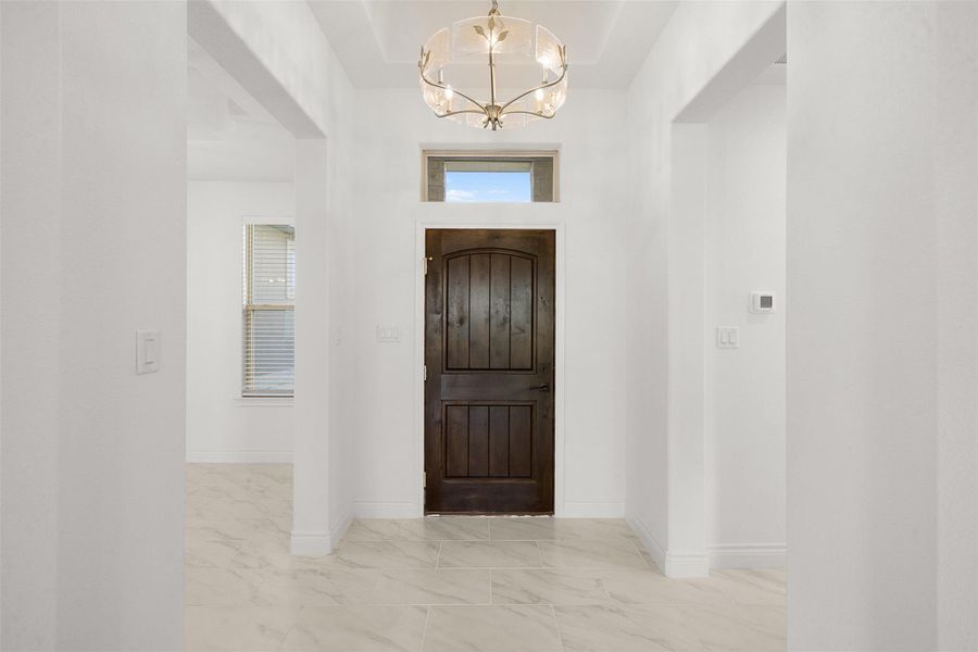 Foyer featuring suspended lighting, light marble finish floors, and plenty of natural light