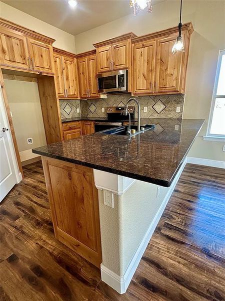 Kitchen featuring kitchen peninsula, dark wood-type flooring, dark stone countertops, hanging light fixtures, and sink