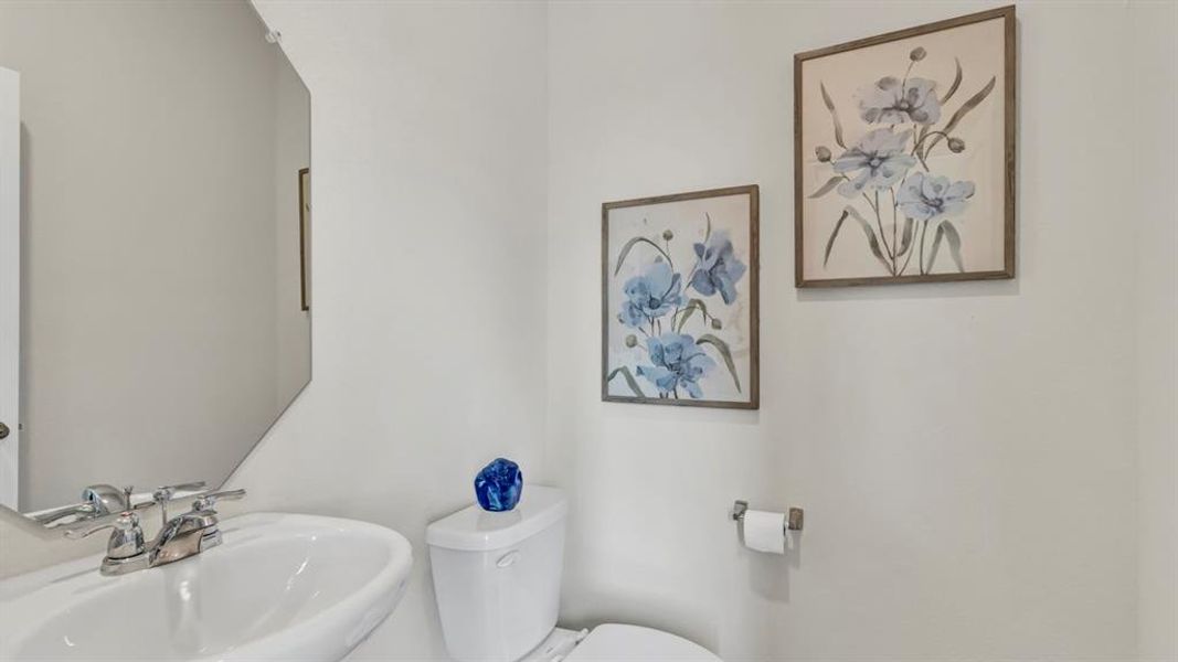 Bathroom featuring a pedestal sink with chrome fixtures, a modern toilet, and a geometric mirror Bathroom featuring a pedestal sink with chrome fixtures, a modern toilet, and a geometric mirror