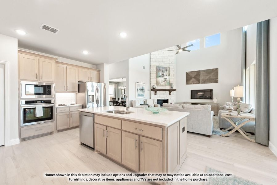 Open-concept kitchen with center island, light wood cabinets, stainless appliances, and adjoining living room with fireplace.