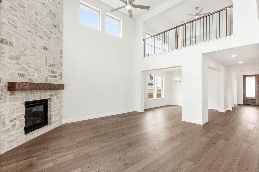 Open living room with two-story ceiling, stone fireplace, hardwood floors, and second-floor balcony overlook