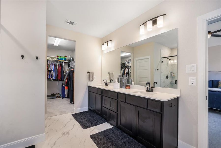 Ensuite bathroom featuring a walk in closet, double vanity, light marble finish flooring, and a stall shower
