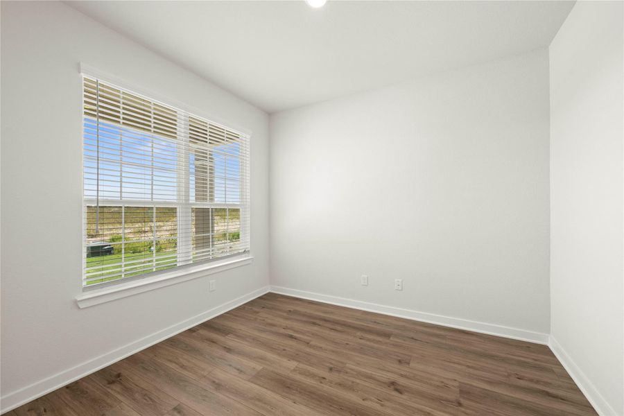 A well-lit room offers expansive views through broad windows with blinds, featuring durable hardwood flooring.