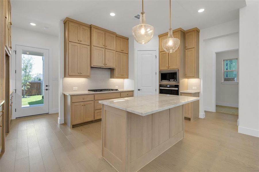 Modern kitchen featuring a central island with a light-toned countertop, light wood-finish cabinetry, and stainless steel appliances